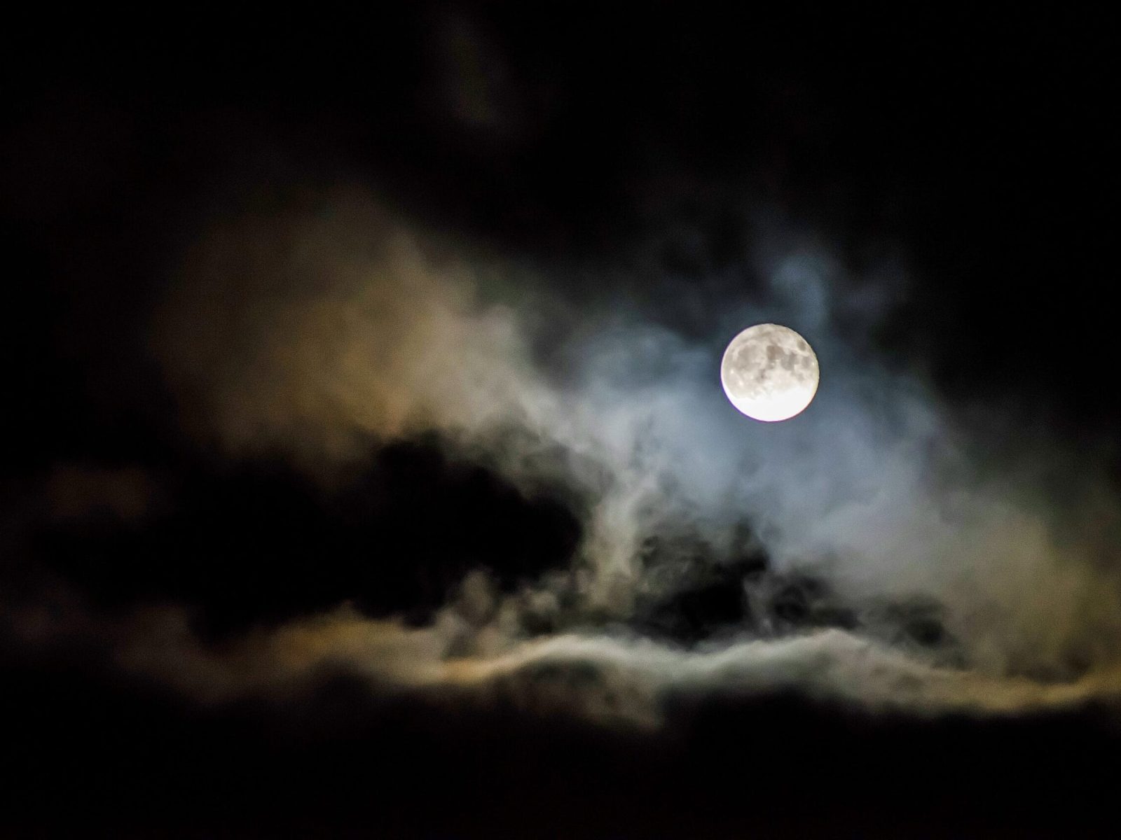 An eerie scene of the moon veiled by ominous clouds in the dark night sky, evoking a sense of mystery and spookiness.